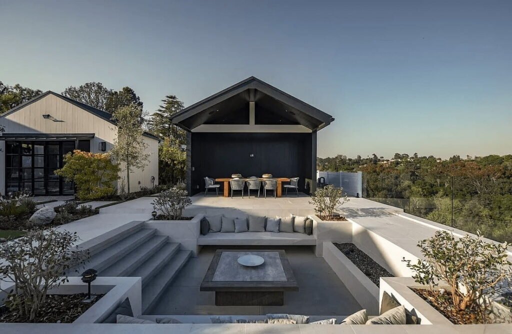 Modern Outdoor Living Space with Sunken Lounge Area A stylish outdoor living space featuring a sunken lounge area with built-in seating, a central coffee table, and a covered dining area with a contemporary design. The space is surrounded by greenery and provides a tranquil setting with scenic views.