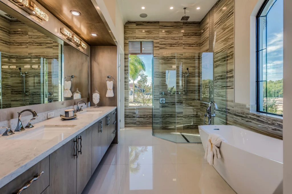 Spacious Modern Bathroom with Marble and Glass Accents Spacious modern bathroom remodel featuring a double vanity with marble countertops, large mirrors, a glass-enclosed shower with marble walls, and a freestanding tub, with views of the outdoors through large windows.